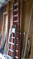 Overview of both ladders leaning against wooden wall; 6 ft step ladder in front, 20 ft orange extension ladder behind