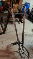 Dark wood handled single wheel hand plow with metal blade and wheel, photographed indoors on concrete floor.