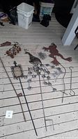 Photo of assorted metal yard art items including animal and decorative garden stakes laid on porch floor