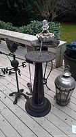Outdoor photo showing sundial on pedestal, weather vane, bird bath with cherub statue, and silver lantern on deck
