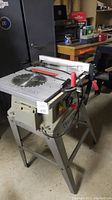 Photo showing Craftsman 10-inch table saw with toothed blade, metal stand, and workshop background.
