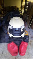 Front view of mower with two red plastic gas cans in foreground