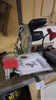 Photo showing the full miter saw unit on a workbench with instruction manual next to it.
