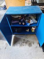 Blue metal garage cupboard with double doors open, showing items on two shelves inside the cupboard.