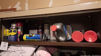 Shelf with household maintenance items including WD-40 can, lubricant cans, oil container, and others.