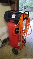 Front view of red vertical Husky air compressor with black top housing, attached orange hose and wheels