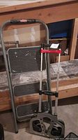 Photo of a folding 3-step Rubbermaid stool and a folding Magna-Cart convertible hand truck leaning against a wooden surface.