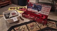 Milwaukee Sawzall in red metal carrying case next to plastic bin with battery charger and signs.