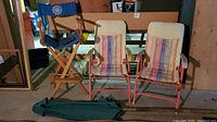 Three folding chairs (two metal frame with striped fabric and one wooden director style) with green folded patio umbrella in front.