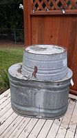 Two galvanized metal tubs stacked one inside the other on a wooden deck outdoors next to a wooden fence.