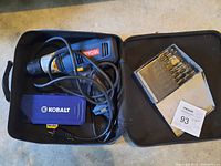 Ryobi electric drill with power cord inside soft black carrying case, Kobalt blue plastic drill bit case, and metal drill bit set box