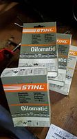 Four boxes of Stihl Oilomatic new in box chainsaw chains with detailed view of one box showing multilingual labeling and chain specifications.