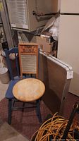 Blue wooden chair with round natural wood seat placed behind the vintage metal and wood washboard branded 'DubL Handy' by Columbus Washboard Co., next to a folding table and other storage items.