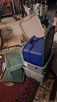 Stacked gray, blue, and clear plastic storage totes with lids visible, placed in a workshop setting.