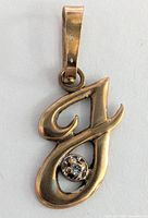Frontal view of the yellow gold letter "J" pendant showing the diamond set in a floral bezel.