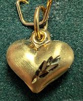 Photo of gold heart pendant showing engraved leaf design on one side.