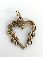 Close-up photo of a 10K yellow gold heart-shaped pendant with floral and leaf details forming an open heart shape and a bail for hanging.