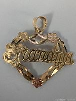 Front view of a 10K yellow gold heart pendant with 'Grandma' scripted in the middle and floral accents on the heart outline.
