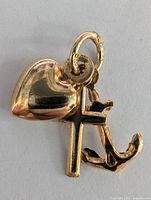 Close-up front view of the 10K yellow gold pendant, showing the heart, cross, and anchor charms hanging from the textured gold loop.