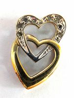 Front view of the pendant showing the two interlinked hearts with diamond accents and polished gold surface.