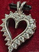 Close-up front view of a heart-shaped pendant in 10K white gold with clear cubic zirconia stones set around the border, polished double loop bail attached.