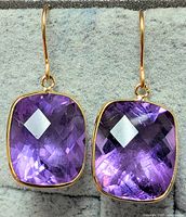 Front-facing photo of the pair of 10K yellow gold drop earrings featuring large cushion cut purple amethyst stones.