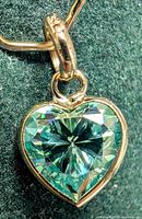 Close-up image of heart-shaped blue moissanite pendant in 10K yellow gold showing details of gemstone and gold setting.