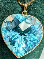 Close-up front view of the heart-shaped blue topaz pendant with 10K gold setting on a dark background.