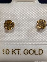 Pair of 10K gold stud earrings with round citrine gemstones mounted in prong settings displayed in packaging marked '10 KT. GOLD'.