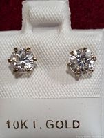 Close-up image of the two stud earrings with clear round cubic zirconia stones in 10K gold prong settings, displayed on white card marked 10KT.GOLD.