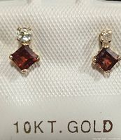 Front view of pair of 10K gold earrings with garnet and diamond stones attached to a white card stamped '10KT. GOLD'