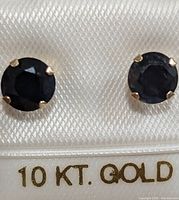 Front view of sapphire stud earrings set in 10K gold prongs displayed on a white backing marked '10 KT. GOLD' in gold lettering.