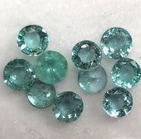 Close-up photo of eleven small round faceted genuine emerald gemstones on a white background, showing their green bluish hues and many facets.