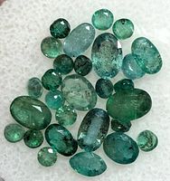 Close-up of various genuine emerald gemstones, showing their green color, different oval and round cuts, and natural inclusions.