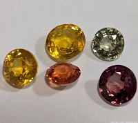 Five genuine fancy color sapphires in yellow, orange, pink, and pale gray, arranged on white background.