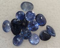 Multiple loose genuine sapphires in various blue shades and shapes on white background showing facets and clarity.