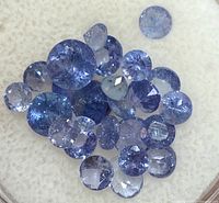 Cluster of 26 loose round faceted tanzanite stones on a light background, showing blue to violet-blue color.