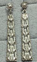 Front view of the pair of silver dangling earrings with textured rectangular links and round stud backings on a grey fabric surface.