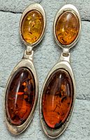 Close-up photo of pair of silver earrings with two oval amber stones each, one lighter and smaller on top, one larger and darker on bottom