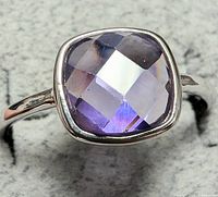 Close-up photo of a sterling silver ring with a faceted cushion-cut amethyst stone.