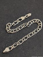 Silver bracelet laid out on a black surface, showing the entire length and design details of the link chain and clasp.