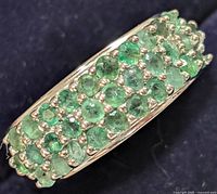 Close-up view of top of silver ring showing three rows of round green emerald stones densely set.