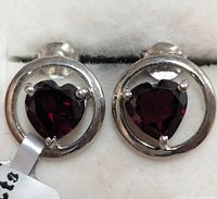 Close-up front view of sterling silver earrings with heart-shaped garnet center stones showing prong settings and shape