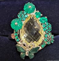 Close-up of ring showcasing pear-shaped lemon quartz center and green carved floral and butterfly accents.