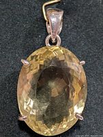 Close-up image of an oval faceted lemon quartz pendant set in silver with four prongs and a silver bail on a black background.