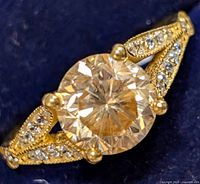 Close-up front view of silver ring with round moissanite center stone and accent stones on split band against dark background.