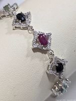 Close-up of the linked sections showing ruby and sapphire stones surrounded by clear stones in silver mounts and small emerald stones.