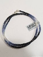 Full view of the necklace showing the faceted blue sapphire beads graduating in color and the silver clasp with the label showing weight.