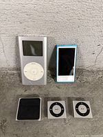 Photo showing all five iPods arranged on concrete: iPod Classic, iPod Touch, iPod Nano, and two iPod Shuffles.