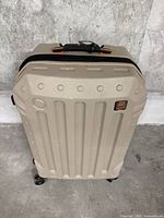 Front view of beige hard shell suitcase with Britbag logo visible, set on concrete floor against a concrete wall.